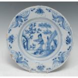An English Delft plate, decorated in underglaze blue with Oriental figure, blossom and building, the