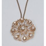 A diamond pendant brooch, scrolling open shaped circular pendant inset with a central round