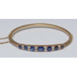 A diamond and sapphire hinge bangle, central crest of seven oval round and cushion cut blue
