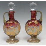 A pair of cranberry liqueur decanters, applied in polychrome and gilt with foliage and