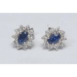 A pair of diamond and sapphire cluster earrings, each with a central oval blue sapphire surrounded