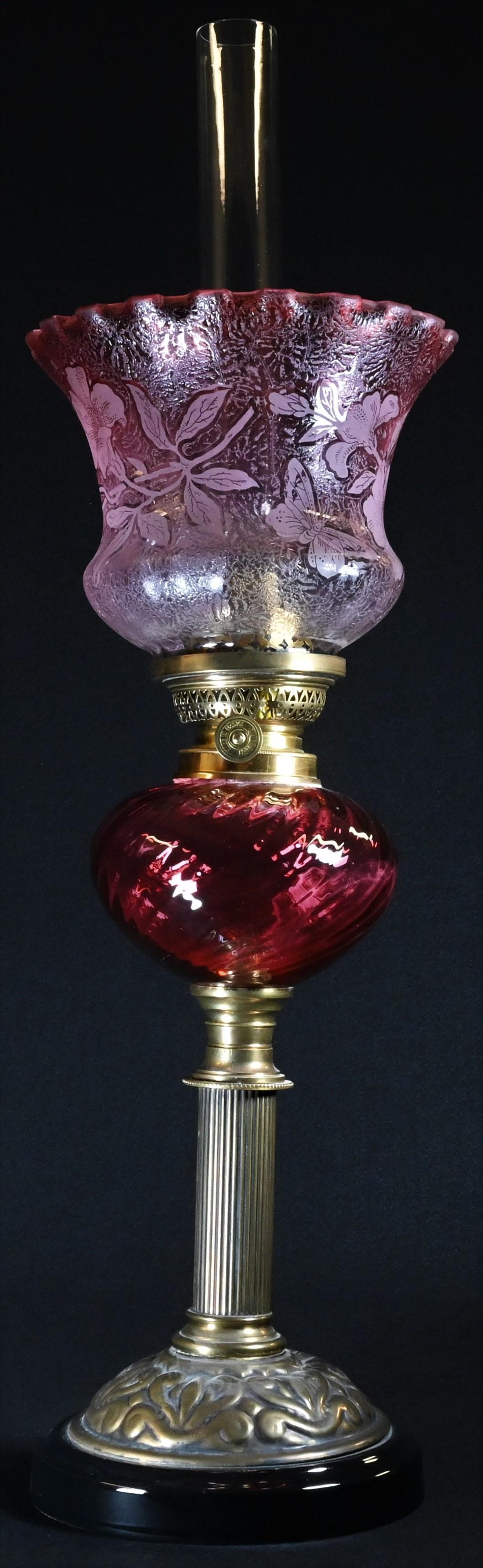 A cranberry glass and brass table oil lamp, Gaudard adjustable burner, the frilled shade frosted and