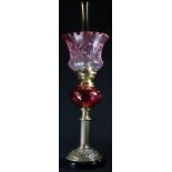 A cranberry glass and brass table oil lamp, Gaudard adjustable burner, the frilled shade frosted and