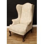 A large George II style mahogany wingback armchair, outswept arms, stuffed over upholstery, acanthus