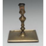 A 17th century French brass candlestick, waisted sconce, knopped stem, broad square base, stump