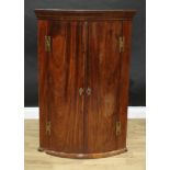 A George III mahogany bow fronted wall hanging corner cupboard, moulded cornice above a pair of