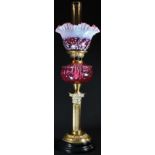 An Edwardian cranberry glass and brass Corinthian column table oil lamp, frilled vaseline shade,