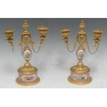 A pair of Sevres and gilt metal candlesticks, painted with musical trophies within gilt cartouches
