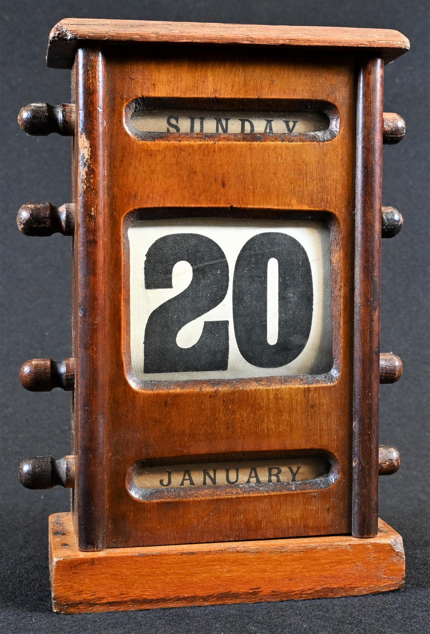 An early 20th century mahogany perpetual desk calendar, oversailing top above glazed apertures for