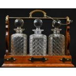 An Edwardian oak three bottle tantalus, canted square hobnail-cut clear glass decanters, spreading