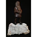 A Black Forest figure, carved as a mountaineering gnome, he stands, atop a quartz boulder, 24.5cm