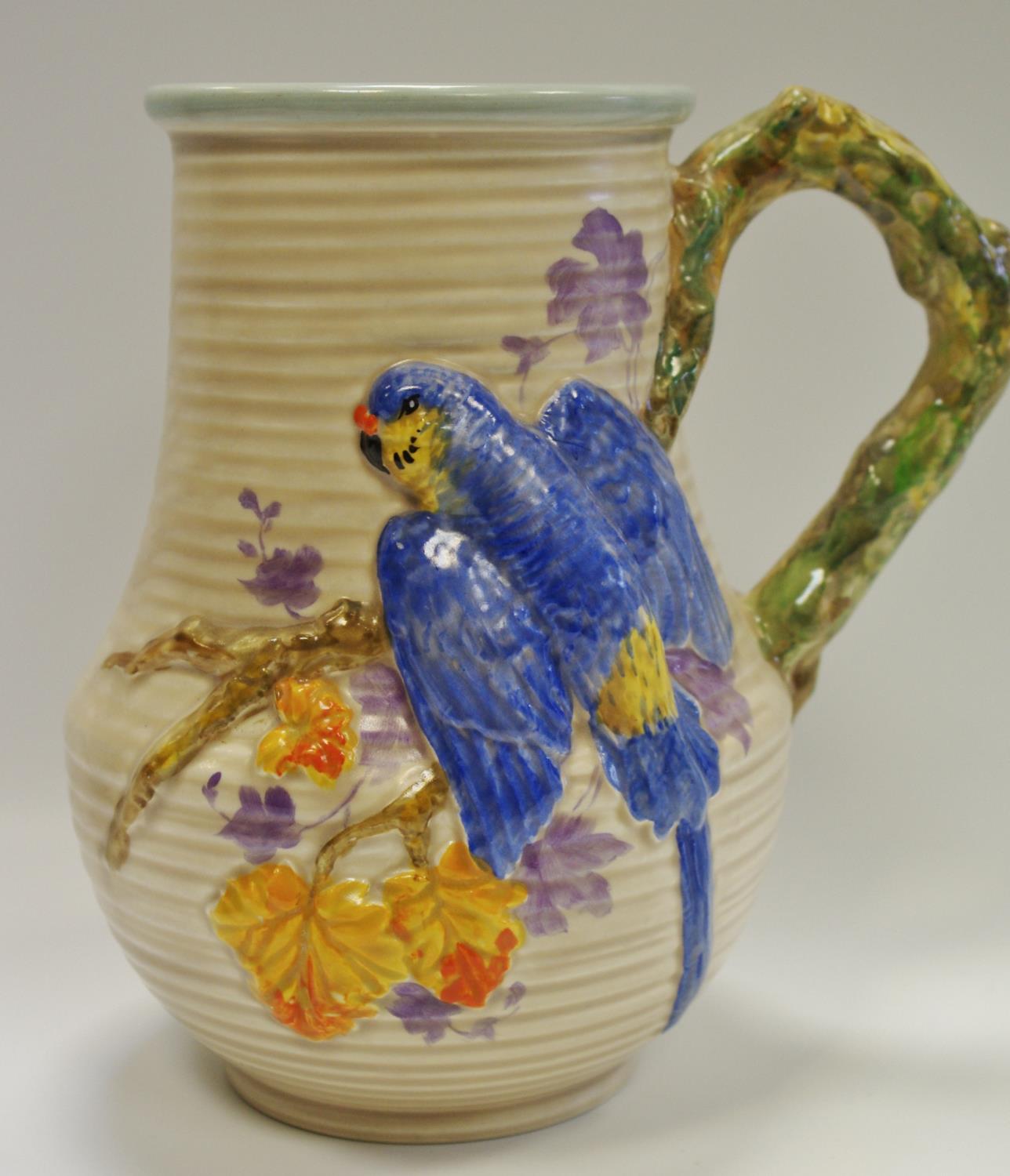 A Clarice Cliff jug moulded in relief with a parrot & foliage, naturalistic handle, ribbed