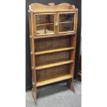 An Arts and Crafts oak book case, shaped top above pair of glazed doors over 3 open shelves, peg