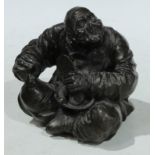 Chinese School, a dark patinated bronze, of an elder, seated, with the tools of his trade, 13cm high