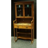 An arts and crafts oak bookcase, outswept cornice above a pair of stained glass doors inclosing