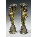 A pair of gilt metal figures, modelled as cherubs/putti standing, each holding a basket of fruit