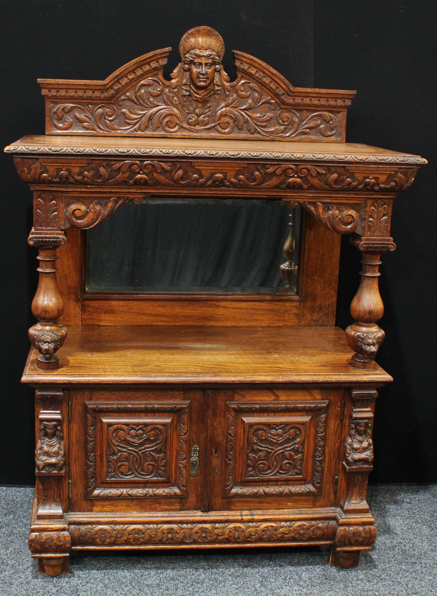 A late Victorian oak pier/side cabinet, arched pediment centred by a carved mask, above a