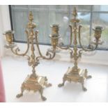 A pair of brass two-light two branch candleabra, cast with leafy scrolls, square bases, paw feet,