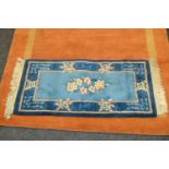 A Chinese woollen runner, with flowers in tones of blue, 120cm x 60cm; a rust woollen rug, banded