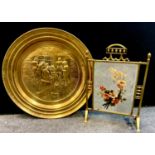An Arts and Crafts painted mirror brass fire screen; a large brass embossed charger.