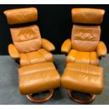 A pair of Ekornes Stressless recliner armchairs and footstools, caramel leather upholstery.