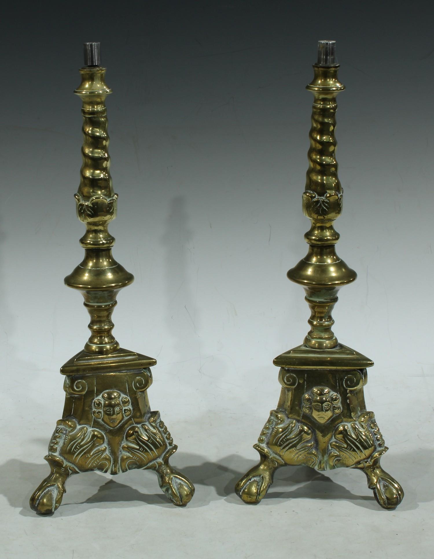 A pair of brass candlesticks, converted for electricity as table lamps, tripod bases, the brass