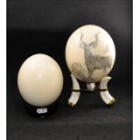 Two ostrich (struthio) eggs on mounts, One decorated with a hand drawn beautiful striped forest