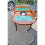 An veneered marquetry games table, the top inlaid with floral foliage lifting away to expose a