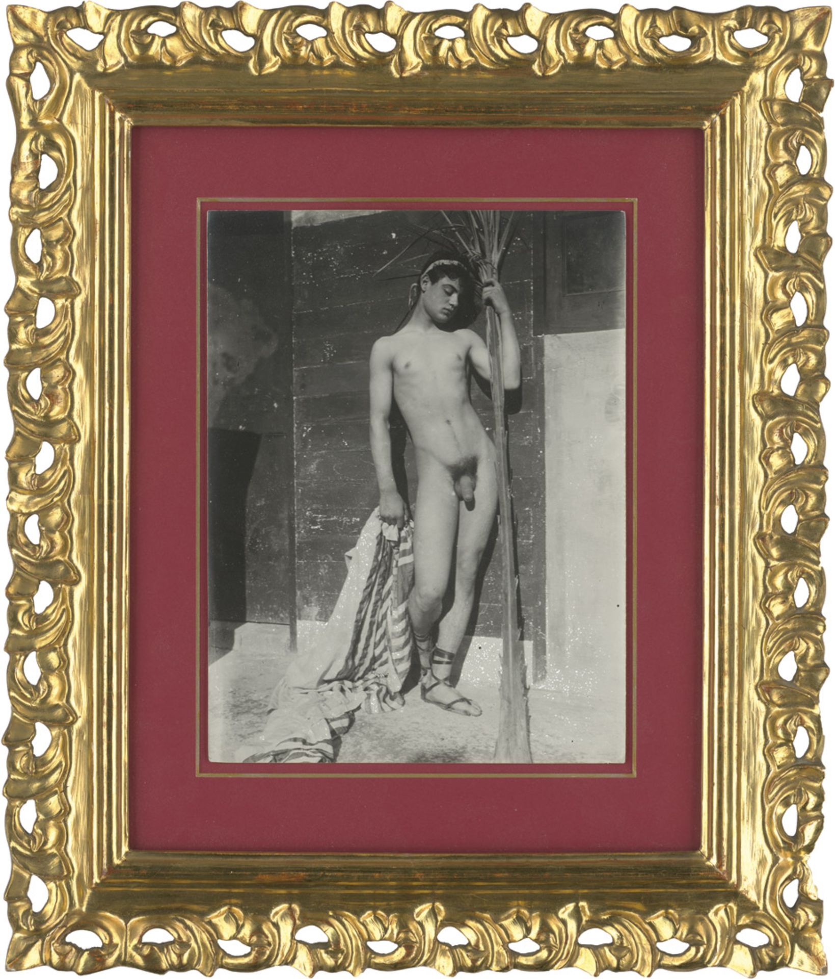 Gloeden, Wilhelm von: Young male nude on terrace with cloth and palm leafYoung male nude on