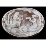 A large oval shell cameo brooch: depicting two maidens serenading a recumbent lion within a plain