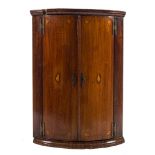 A mid 18th Century mahogany and inlaid bow-fronted hanging corner cupboard:, with a moulded cornice,