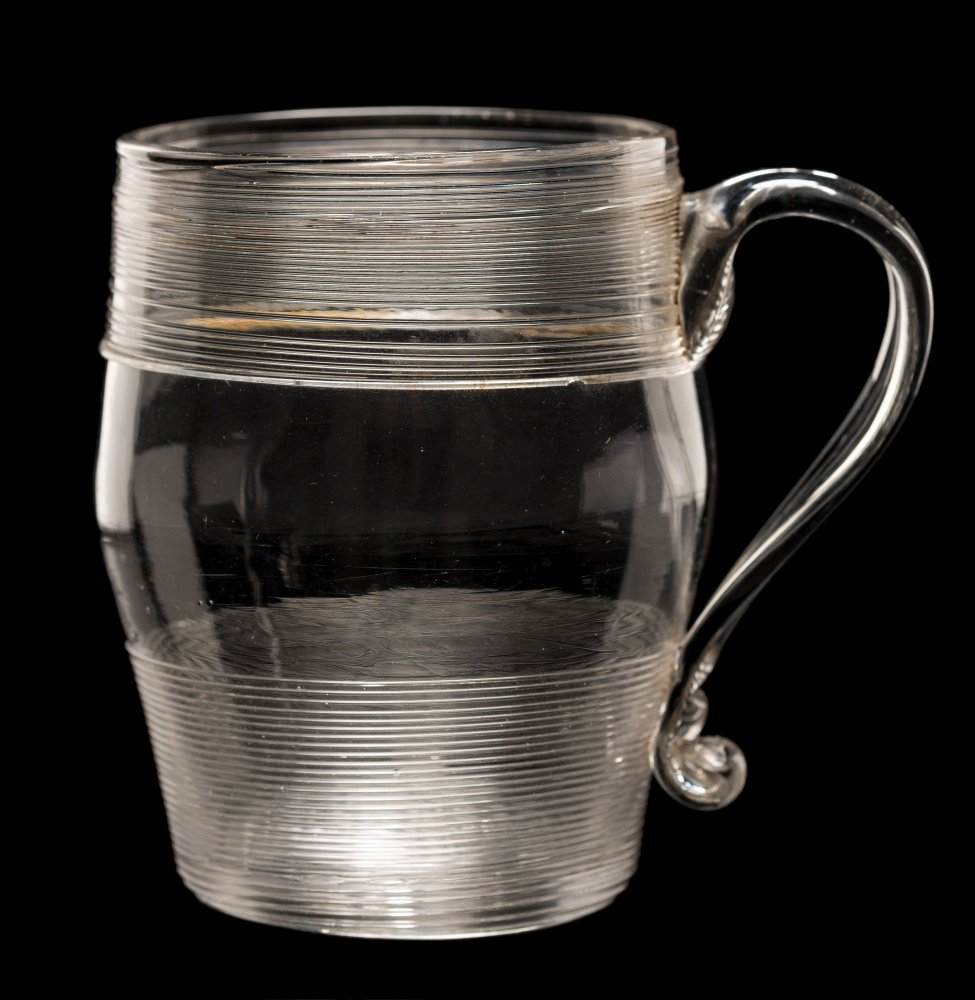 An English glass tankard: of barrel shaped form with strap handle decorated below the rim and above