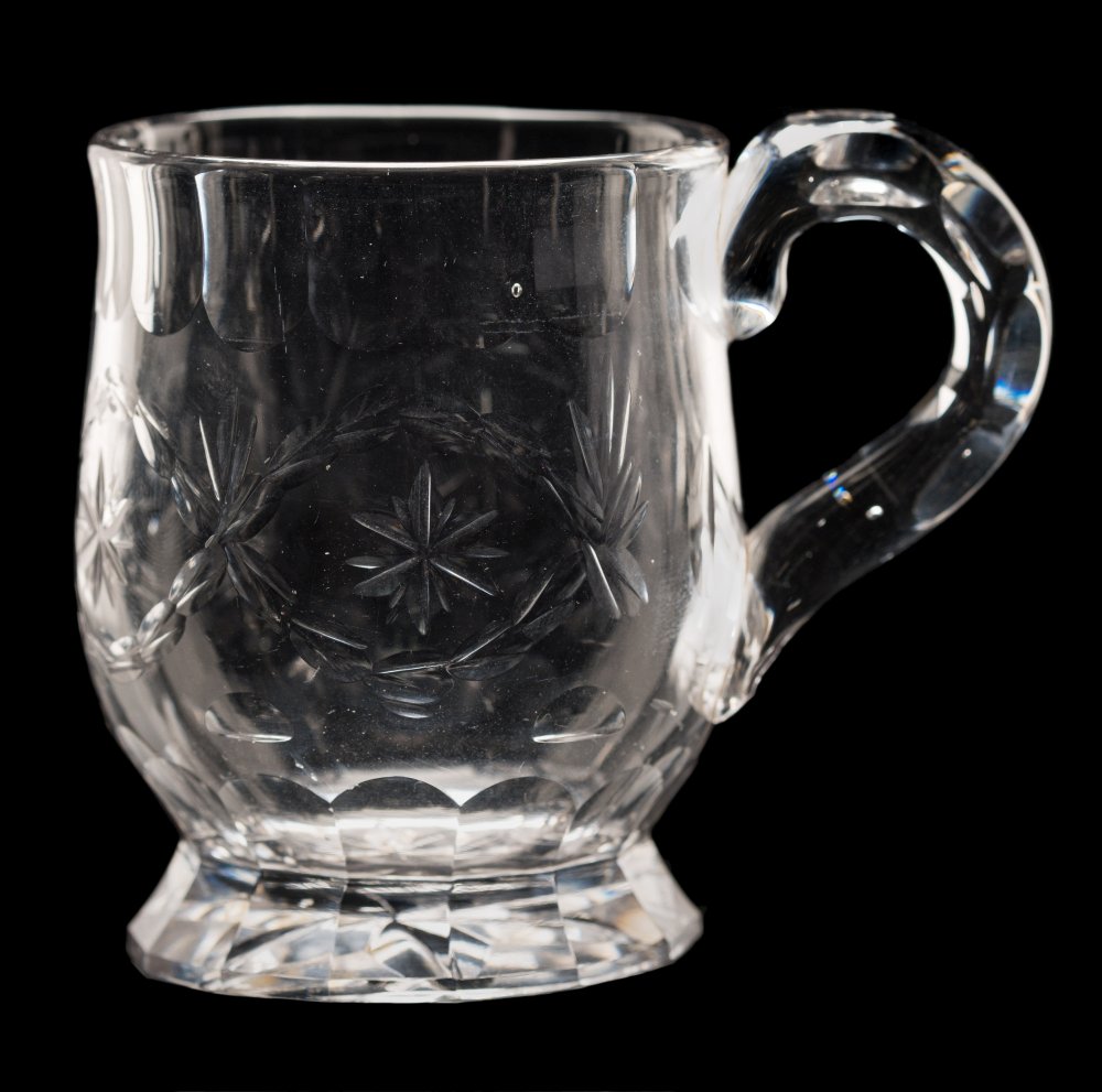 A small clear glass mug: of thistle shaped form with facet cut handle and slice cut rim and foot,