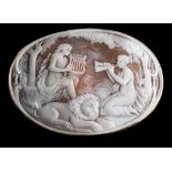 A large oval shell cameo brooch: depicting two maidens serenading a recumbent lion within a plain