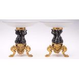 A pair of bronze and gilt bronze tazze: the opaque circular glass dishes mounted on three cherub