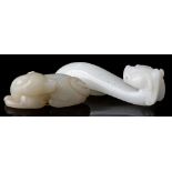 A Chinese celadon jade carving of a dog and a dragon belt hook: the dog recumbent with its head