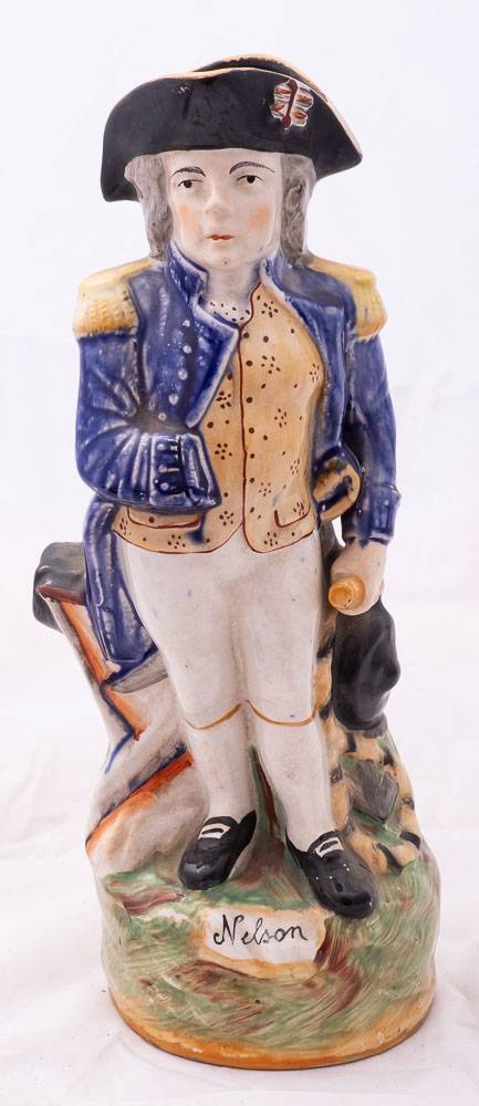 A Staffordshire character jug modelled as Admiral Lord Nelson: standing beside a cannon and holding