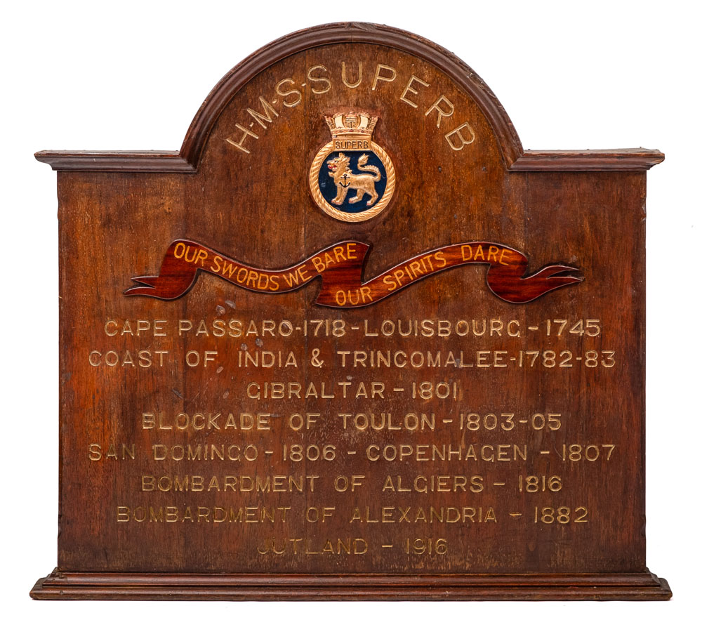 A carved oak honours board for HMS Superb: the arched top above ship's name and badges with action