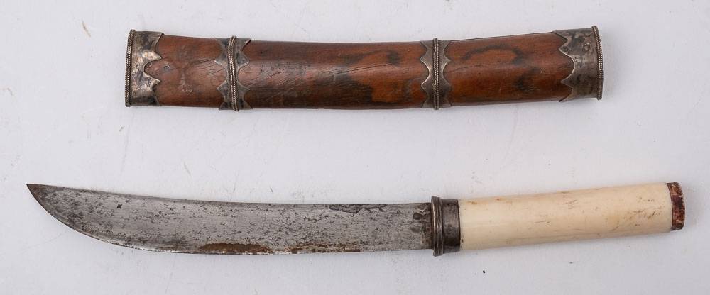 A Burmese dha dagger: the short curved back blade over a white metal hilt and one piece ivory grip,