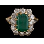 An emerald and diamond cushion-shaped cluster ring: with central rectangular emerald 10.