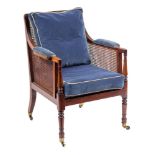 A Regency mahogany library Bergere armchair:, with a reeded frame, having a curved cane panel back,