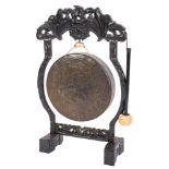 A circular hammered brass gong on a Chinese carved hardwood stand:,