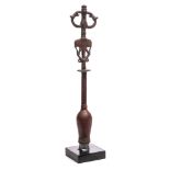 A bronze staff head : surmounted by an idol, on a knopped stem and square plinth base,