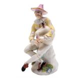 A Meissen figure of Harlequin: modelled after Kandler, seated cross legged playing the bagpipes,