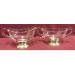 A 2 handled clear glass sugar bowl with matching cream jug, both raised on sterling silver feet.