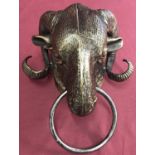 A bronzed cast metal rams head with ring.