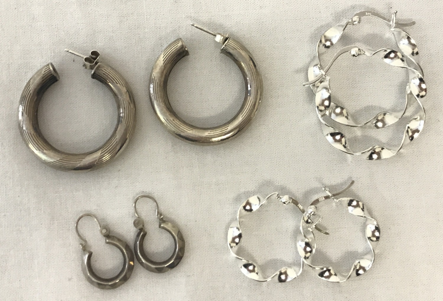 4 pairs of silver and white metal hoop style earrings.