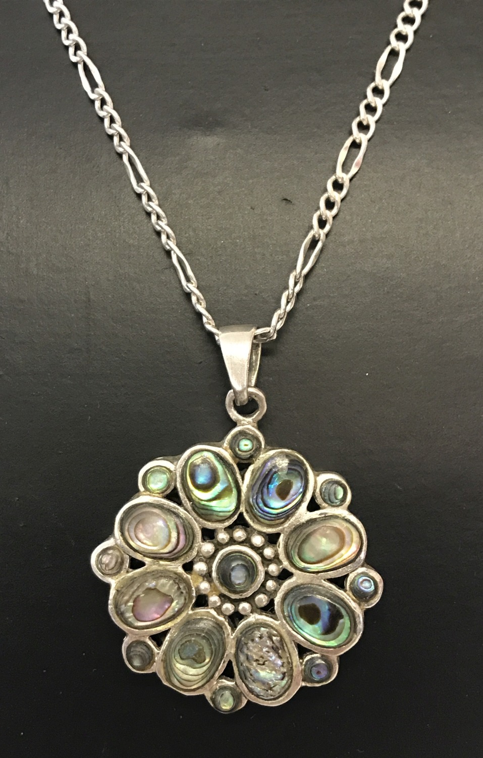 A flower design silver pendant set with oval and round cut paua shell. On a silver 20" figaro chain.