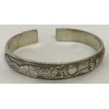 A Chinese white metal bangle with dragon and phoenix detail.