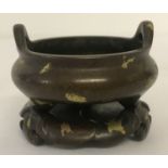A miniature Chinese bronze 3 footed censer, with gold splatted detail, on a stand.